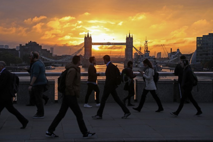 Commuters walk across London Bridge against a backdrop of Tower Bridge.