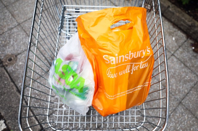 An Asda plastic carrier bag, left, and a Sainsbury's plastic carrier bag, right, sit in a supermarket trolley in this arranged photograph in Watford, U.K.